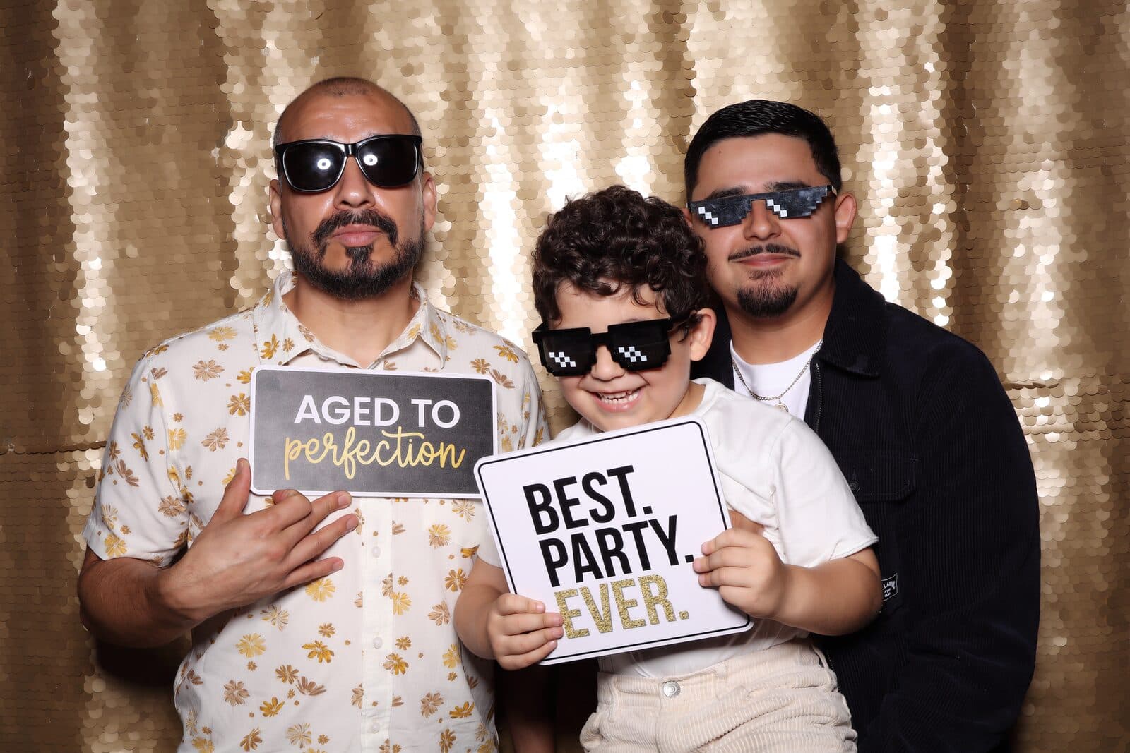 Guests in playful sunglasses holding party signs at the Shutter Bar photo booth